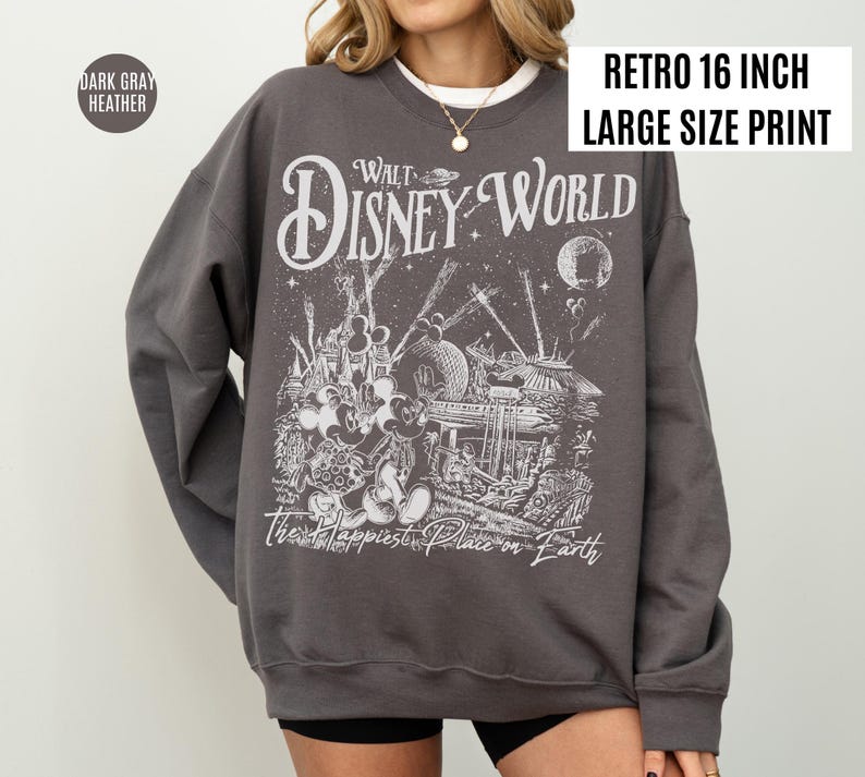 Peut inclure: Sweat-shirt gris fonc&eacute; chin&eacute; avec une impression r&eacute;tro de grande taille de 16 pouces. Le graphisme pr&eacute;sente les mots "Walt Disney World" et "The Happiest Place on Earth" avec une illustration d&eacute;taill&eacute;e de Mickey Mouse.