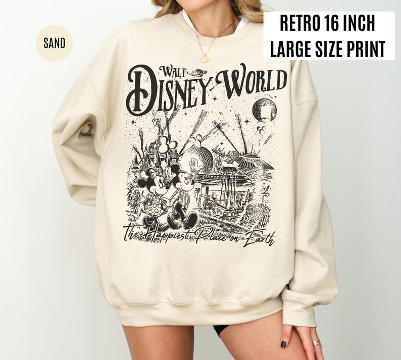 Peut inclure: Sweat-shirt couleur sable avec un motif noir et blanc de Walt Disney World, Mickey et Minnie Mouse, et le texte "The Happiest Place on Earth". Le sweat-shirt a un col rond et des manches longues. Le texte "Retro 16 inch Large Size Print" est &eacute;galement visible.