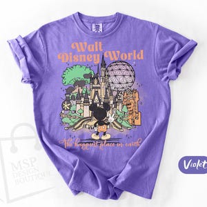 May include: Violet t-shirt featuring a colorful graphic of Walt Disney World with Mickey Mouse. The design includes the text "Walt Disney World" and "The happiest place on earth". The shirt is a crew neck.