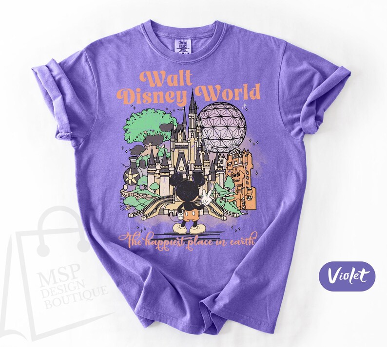 May include: Violet t-shirt featuring a colorful graphic of Walt Disney World with Mickey Mouse. The design includes the text "Walt Disney World" and "The happiest place on earth". The shirt is a crew neck.