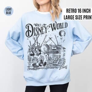 Peut inclure: Sweat-shirt bleu clair avec un imprim&eacute; graphique r&eacute;tro de Walt Disney World. Le motif noir et blanc repr&eacute;sente Mickey et Minnie Mouse, des attractions du parc et le texte "The Happiest Place on Earth". L'impression est de grande taille.