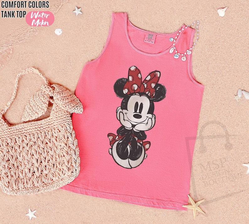 May include: A watermelon pink Comfort Colors tank top featuring a graphic print of Minnie Mouse with a red and white polka dot bow. The tank top has a round neckline and sleeveless design. Text on the garment reads Comfort Colors Tank Top.