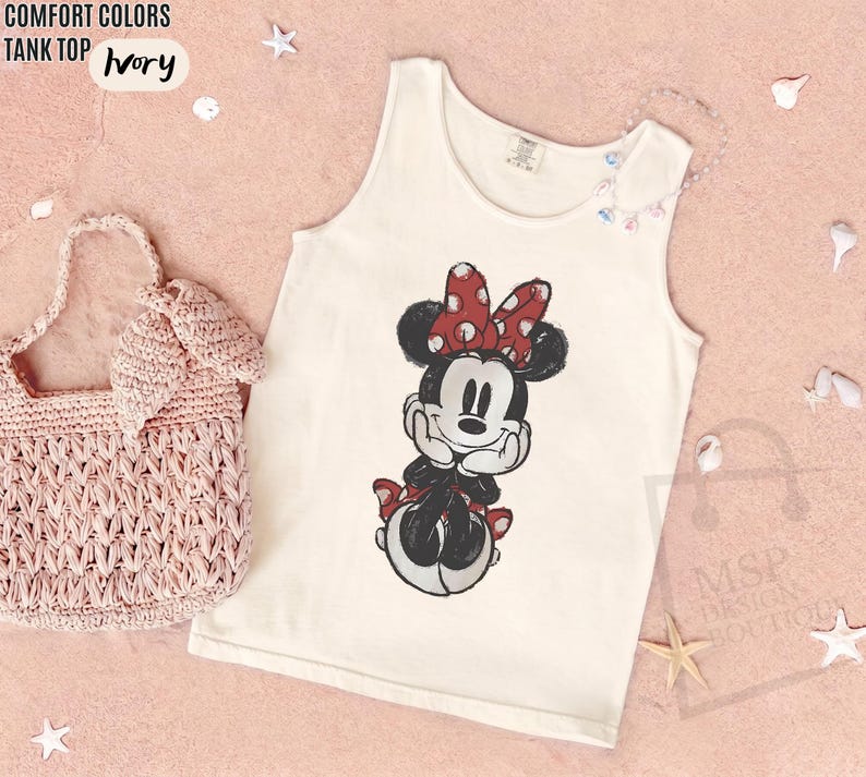 May include: An ivory tank top featuring a graphic print of Minnie Mouse with a red and white polka dot bow. The tank top is displayed alongside a light pink crocheted handbag. Text on the image reads COMFORT COLORS TANK TOP IVORY and MSP DESIGN BOUTIQUE.