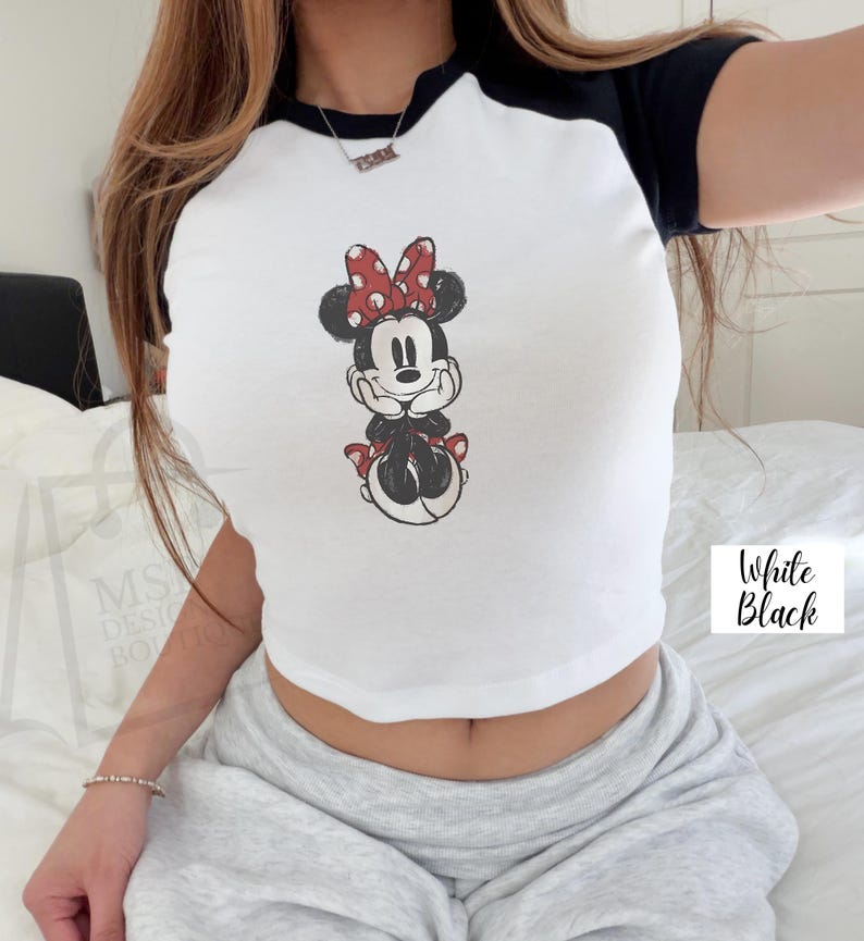 May include: White and black raglan crop top featuring a Minnie Mouse graphic. The graphic shows Minnie Mouse with a red bow and red accents. The text "White Black" is in the lower right corner.