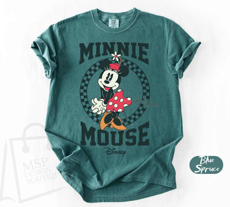 May include: Teal-colored t-shirt featuring a graphic of Minnie Mouse. The design includes Minnie in a red and white polka-dot dress, a flower on her head, and the words "MINNIE MOUSE" in bold, black letters. The Disney logo is also visible.