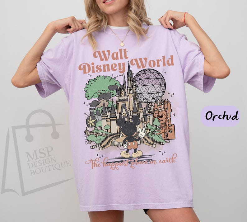 May include: Orchid-colored t-shirt with a graphic of Walt Disney World. The design includes a castle, Spaceship Earth, and Mickey Mouse. Text reads "Walt Disney World" and "the happiest place on earth."
