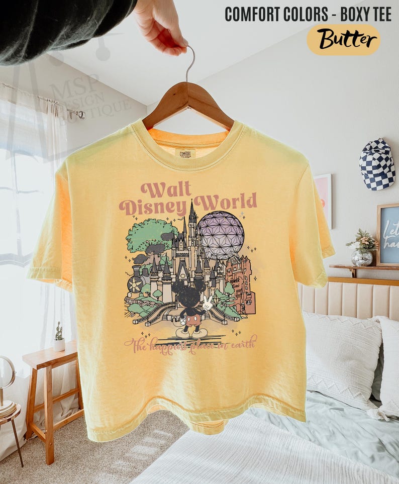 May include: Yellow Comfort Colors boxy tee featuring a graphic of Walt Disney World with Mickey Mouse. The text on the shirt reads "Walt Disney World" and "The happiest place on earth".