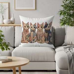 Four patchwork cats with bows and heart charm sit on a white pillow.