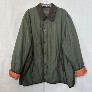 May include: Olive green quilted jacket with a brown corduroy collar and orange cuffs. The jacket has a button-up front, two zippered pockets, and brown trim. A classic outerwear piece.