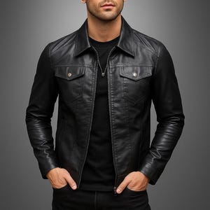 Op de afbeelding: Zwarte leren jas met een kraag, twee borstzakken en een ritssluiting. De jas heeft een klassiek ontwerp en wordt over een zwart shirt gedragen. Het model draagt een zwarte jeans en heeft de handen in de zakken.