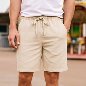 Puede incluir: Pantalones cortos color caqui con cintura elástica y cordón. Los pantalones cortos están hechos de una tela clara y tienen bolsillos. El modelo lleva una camiseta blanca. Ropa casual de verano.