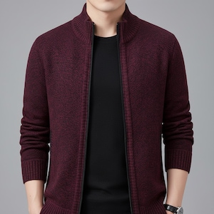 May include: A burgundy zip-up sweater with a high collar. The sweater has a textured knit pattern and a black zipper. The sleeves are long and end with ribbed cuffs. The person in the image is wearing a black shirt underneath.
