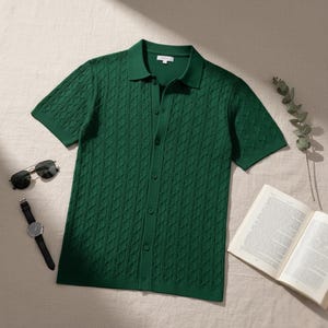 May include: A green short-sleeved polo shirt with a textured cable knit pattern. The shirt has a button-down front and a collared neckline. Sunglasses, a watch, and an open book are also visible.