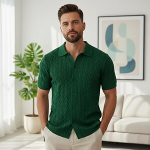 May include: A green short-sleeve polo shirt with a textured cable knit design. The shirt has a button-down front and a collared neckline. The model is wearing the shirt with beige pants.