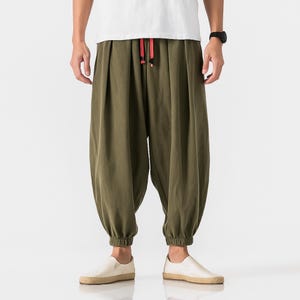 May include: Olive green harem pants with a drawstring waist and elastic cuffs. The pants have a loose, comfortable fit and are paired with white slip-on shoes. The drawstring is red.