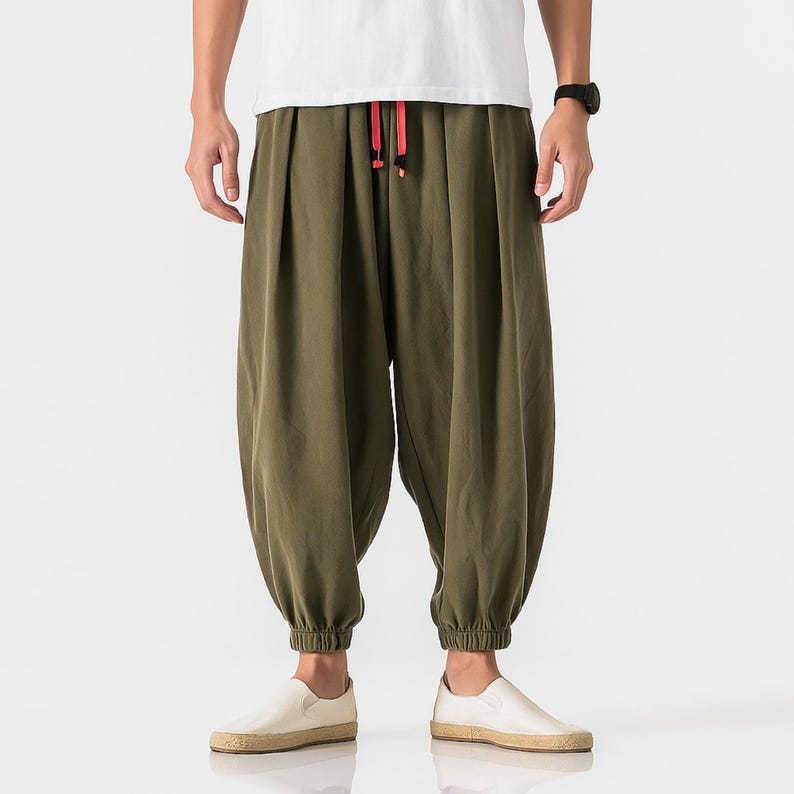 May include: Olive green harem pants with a drawstring waist and elastic cuffs. The pants have a loose, comfortable fit and are paired with white slip-on shoes. The drawstring is red.