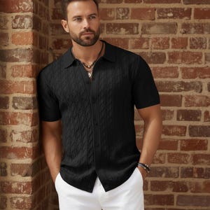 May include: A black short-sleeve button-down shirt with a textured cable knit design. The shirt has a collared neckline and is paired with white pants. The model is standing in front of a brick wall.