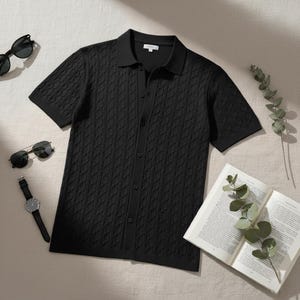 May include: Black short-sleeve polo shirt with a textured cable knit pattern. The shirt has a button-down front and a classic collar. Sunglasses, a watch, and an open book are also visible.