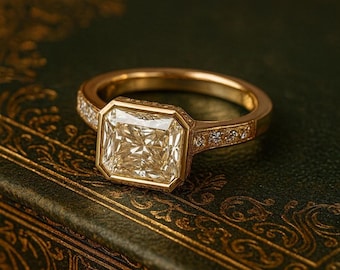 May include: A gold ring with a large, square-cut diamond as the centerpiece. The ring's band is also adorned with smaller diamonds. The ring is set against a dark green background, creating a luxurious and elegant aesthetic.
