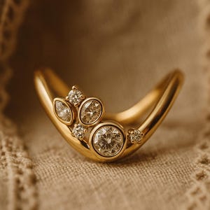 May include: A curved gold ring with several clear, sparkling diamonds. The ring has a smooth, polished finish and is set against a neutral background. The diamonds are of varying sizes and shapes, adding visual interest to the piece.
