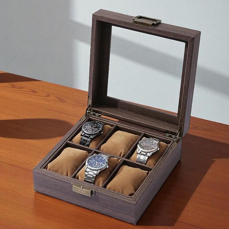 May include: A wooden watch display case with a glass top, showcasing six watches. The case is open, revealing brown watch pillows. Three watches with silver bands and three with black bands are visible.