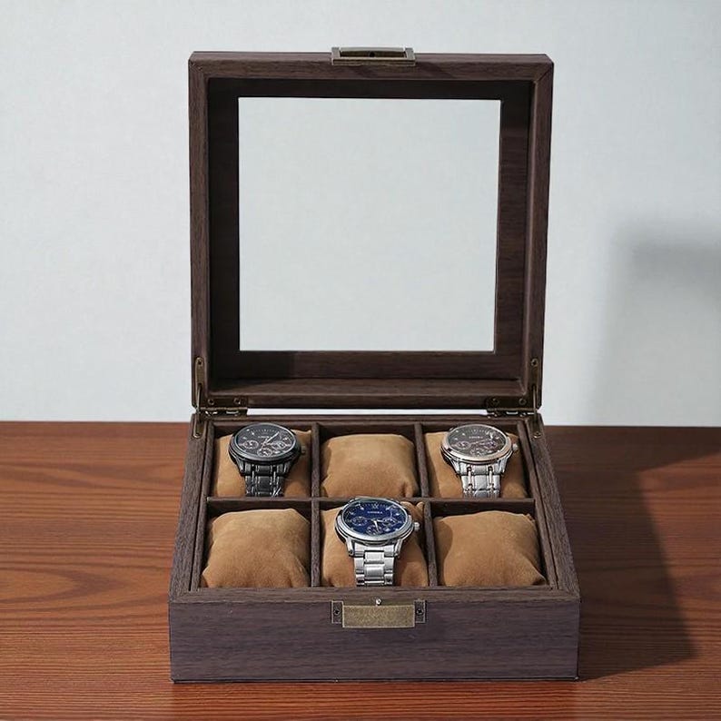 May include: A wooden watch display case with a glass top, showcasing six watches on brown cushions. The case is open, revealing the watches with various metal bands and faces. The wood has a dark brown finish.