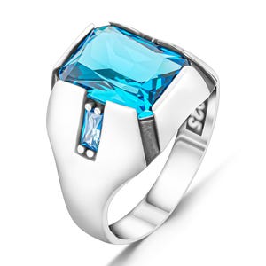 Pode incluir: Anel de prata com uma grande pedra preciosa retangular azul clara. Uma pedra azul retangular menor est&aacute; definida abaixo. O anel tem um design geom&eacute;trico moderno com um acabamento polido.