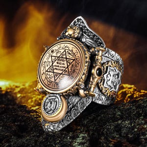 May include: An ornate silver ring with gold detailing. The ring showcases a central circular emblem with a star and script, surrounded by detailed patterns and a crescent moon. The ring has a vintage, elaborate design.