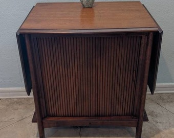 May include: A dark brown wooden cabinet with a sliding door. The cabinet has a top surface and is sitting on a light gray concrete floor. A glass owl figurine is on top of the cabinet.