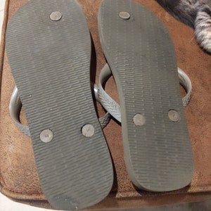 May include: A pair of gray flip-flops with a textured sole and black dots on the bottom.
