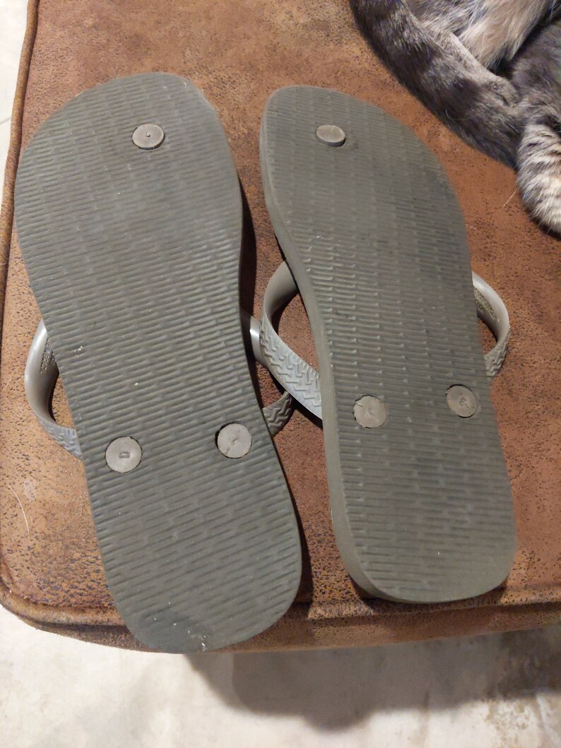May include: A pair of gray flip-flops with a textured sole and black dots on the bottom.