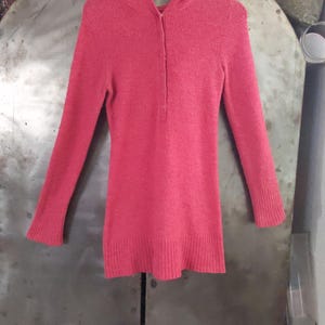 May include: A pink hooded sweater with a button-up front. The sweater is made of a soft, fuzzy material.