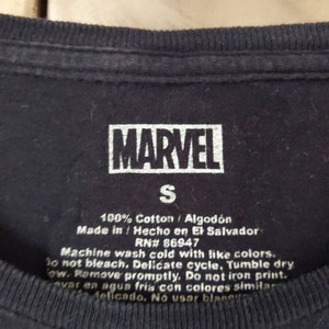 Puede incluir: Una camiseta negra con un logotipo MARVEL blanco y una etiqueta de talla S. La etiqueta tambi&eacute;n incluye instrucciones de cuidado: 100% algod&oacute;n / Algod&oacute;n, Hecho en/Hecho en El Salvador, RN# 86947, Lavar a m&aacute;quina con agua fr&iacute;a con colores similares. No usar blanqueador. Ciclo delicado. Secar en secadora a baja temperatura. Retirar r&aacute;pidamente. No planchar la impresi&oacute;n. Lavar en agua fr&iacute;a con colores similares. Delicado. No usar blanqueador.