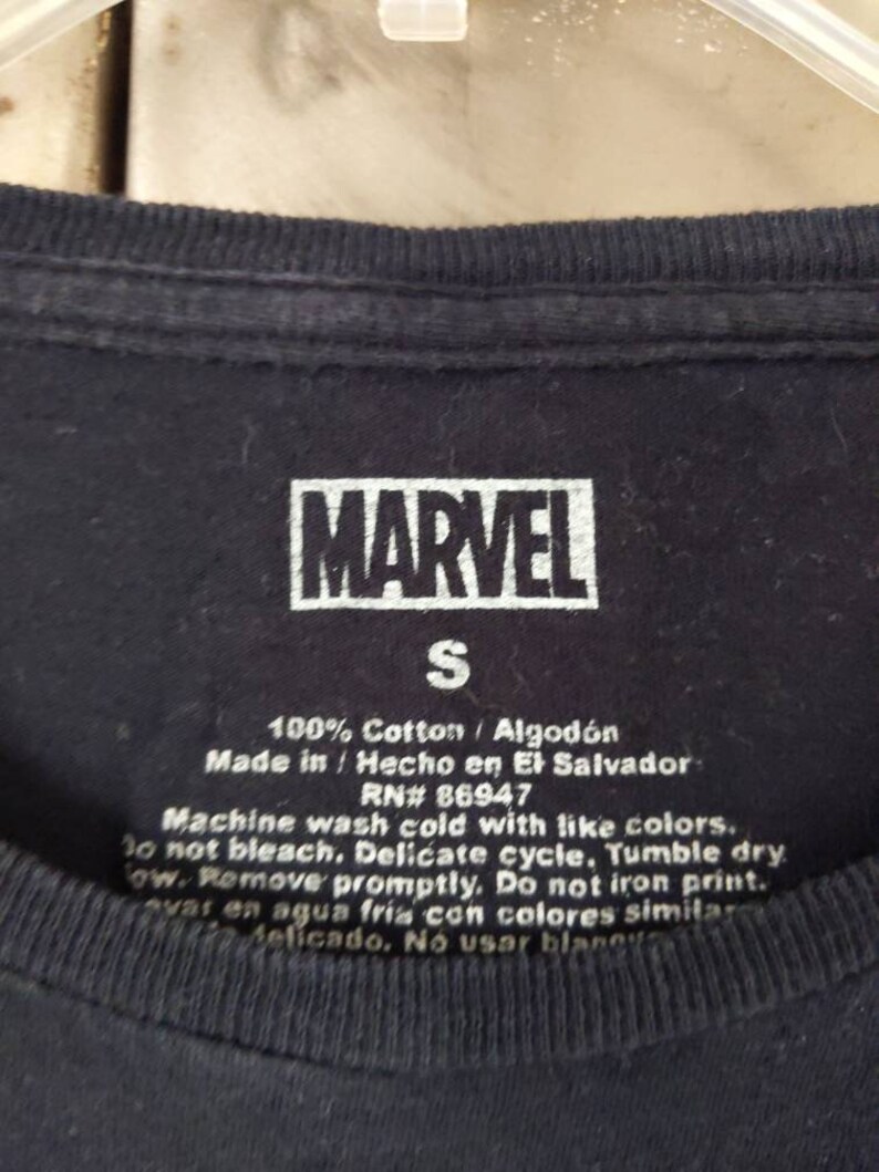 Puede incluir: Una camiseta negra con un logotipo MARVEL blanco y una etiqueta de talla S. La etiqueta tambi&eacute;n incluye instrucciones de cuidado: 100% algod&oacute;n / Algod&oacute;n, Hecho en/Hecho en El Salvador, RN# 86947, Lavar a m&aacute;quina con agua fr&iacute;a con colores similares. No usar blanqueador. Ciclo delicado. Secar en secadora a baja temperatura. Retirar r&aacute;pidamente. No planchar la impresi&oacute;n. Lavar en agua fr&iacute;a con colores similares. Delicado. No usar blanqueador.