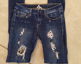 May include: Distressed blue denim jeans with several rips and tears throughout the fabric.