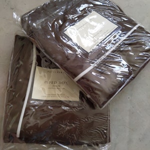 May include: A brown piped box sham pillow cover with white piping. The cover is packaged in plastic and has a label that reads "Piped Box Sham, Couvire-Housse, Euro/Format: 26 x 26 inches (66 x 66 cm)".