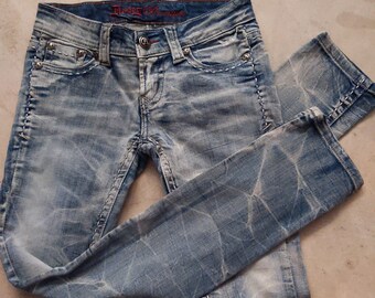 May include: Light blue denim jeans with a faded, distressed look. The jeans have a light wash and a slim fit. The waistband has a red embroidered label that reads "Rock & Republic".