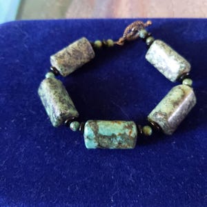 May include: A turquoise and black beaded bracelet with a copper clasp. The beads are cylindrical and have a mottled pattern.