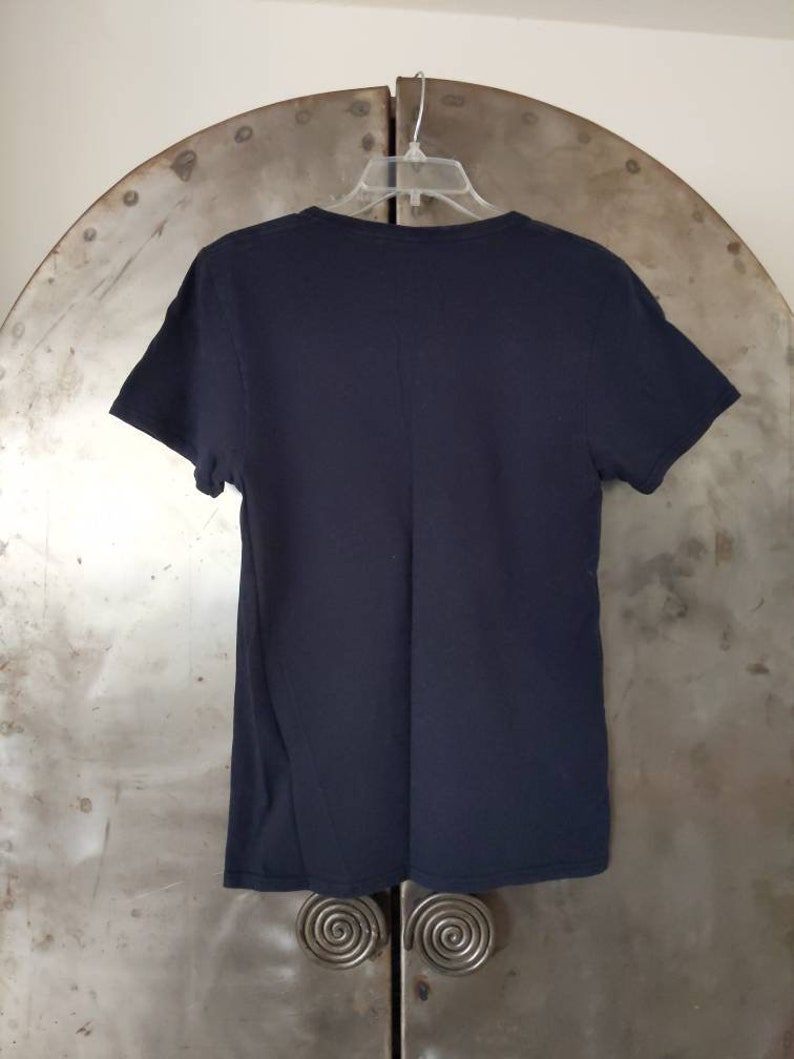 Puede incluir: Una camiseta negra lisa de cuello en V colgada de una percha. La camiseta est&aacute; hecha de una tela suave y c&oacute;moda.