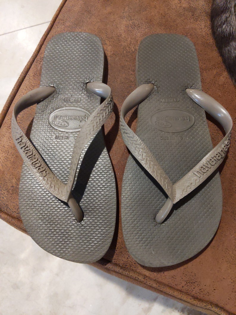 May include: A pair of gray flip-flops with the brand name "havaianas" printed on the straps. The flip-flops have a textured sole and a simple design.