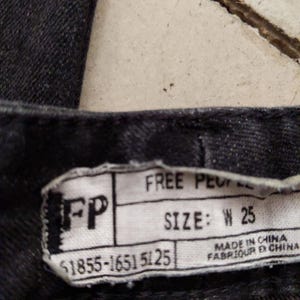 Puede incluir: Vaqueros de mezclilla negros con una etiqueta de Free People. La etiqueta tiene el texto "FP" y "SIZE: W 25" y los n&uacute;meros "$1855-1651 5125". La etiqueta tambi&eacute;n dice "MADE IN CHINA" y "FABRIQUER EN CHINA".