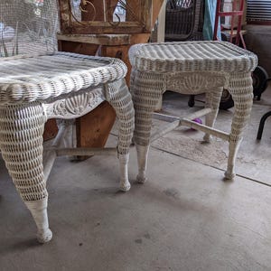 May include: Two white wicker end tables with intricate woven details. The tables have a square top and four legs.