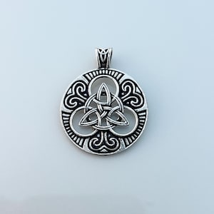 May include: Silver-toned Celtic knot pendant. The pendant features a central triquetra knot design within a circular frame with ornate detailing. The bail is a simple loop. The pendant is likely made of metal.