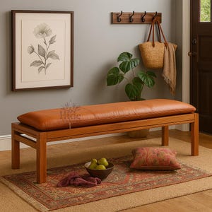 May include: A wooden bench with a rectangular, caramel-colored leather cushion. The bench sits on a patterned rug, with a framed floral print on the wall. A woven bag and scarf hang on a hook rack above.