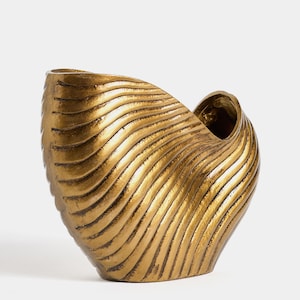 May include: A gold-colored, decorative vase with a unique, shell-like design. The vase features a textured surface with horizontal, wave-like ridges. The opening is a smooth, curved shape. The vase is likely made of metal or a similar material.