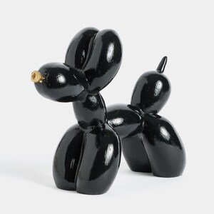 Può includere: Una scultura di cane a palloncino nero lucido con un naso color oro. Il cane è raffigurato in posizione eretta, con il corpo formato da forme arrotondate e gonfie. La scultura ha una superficie riflettente ed è ambientata su uno sfondo bianco.