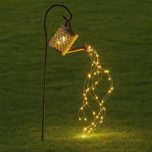 Puede incluir: Estaca decorativa para jardín con diseño de regadera. La regadera de metal tiene un patrón de celosía y está iluminada con luces LED blancas cálidas que caen como agua. La estaca está colocada en una zona de césped.