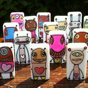 May include: A collection of 20 hand-painted ceramic figurines, each depicting a unique cartoon character with a whimsical design. The figurines are white with colorful details and feature various expressions, including smiling, winking, and surprised. They are all standing upright and have a heart-shaped design on their chest.