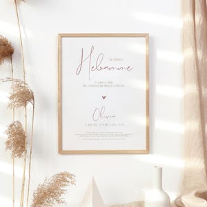 Può includere: Una stampa incorniciata con la parola "Hebamme" in corsivo. La stampa include il nome "Olivia" e i dettagli della sua data di nascita, ora e misure. La cornice è marrone chiaro e lo sfondo è bianco.