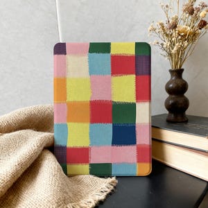 May include: A rectangular case with a vibrant patchwork pattern. The design incorporates squares of different colours, such as pink, yellow, blue, green, and orange. The case is displayed against a neutral backdrop with a vase of dried flowers.